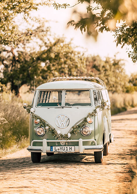 Romantisch dekorierter VW Bulli in Pastellgrün, perfekt als Hochzeitsauto, auf einer idyllischen Landstraße.